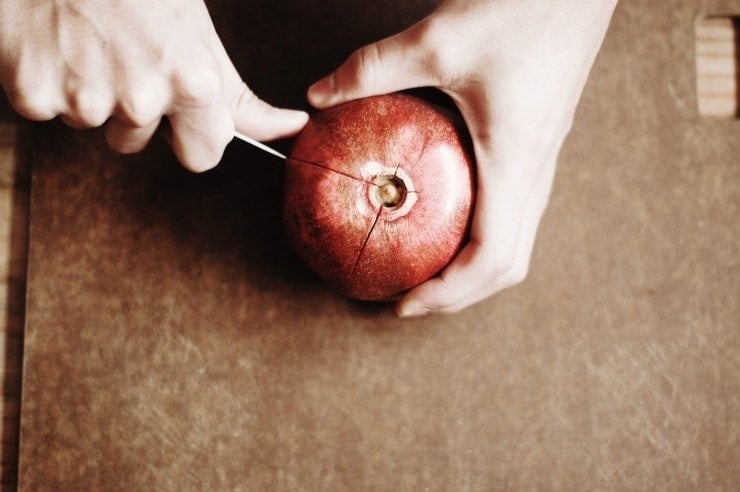 Cutting a pomegranate fruit into sections with a paring knife