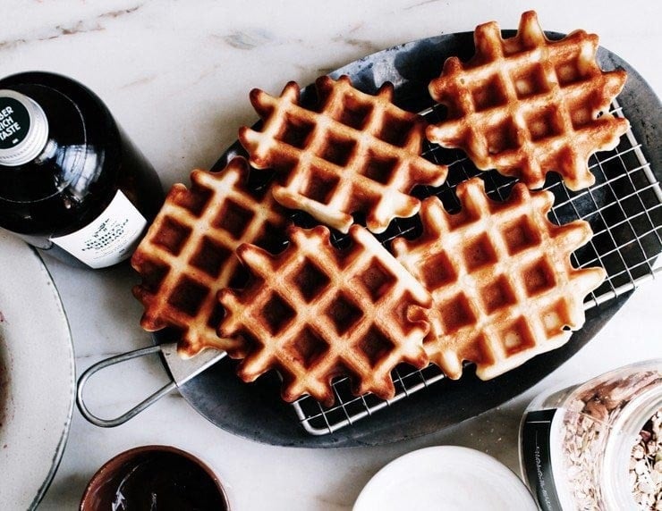 Homemade Belgian waffles on a platter with maple syrup on the side.